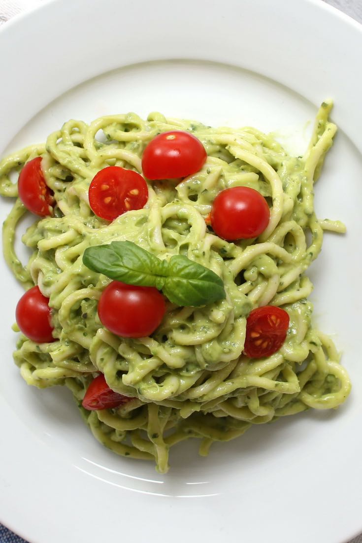 This is an overhead photo of Avocado Pasta on a plate with cherry tomatoes and basil on top