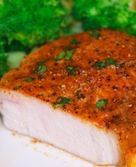 Cross-section of a baked boneless pork chop cut open on a serving plate with broccoli