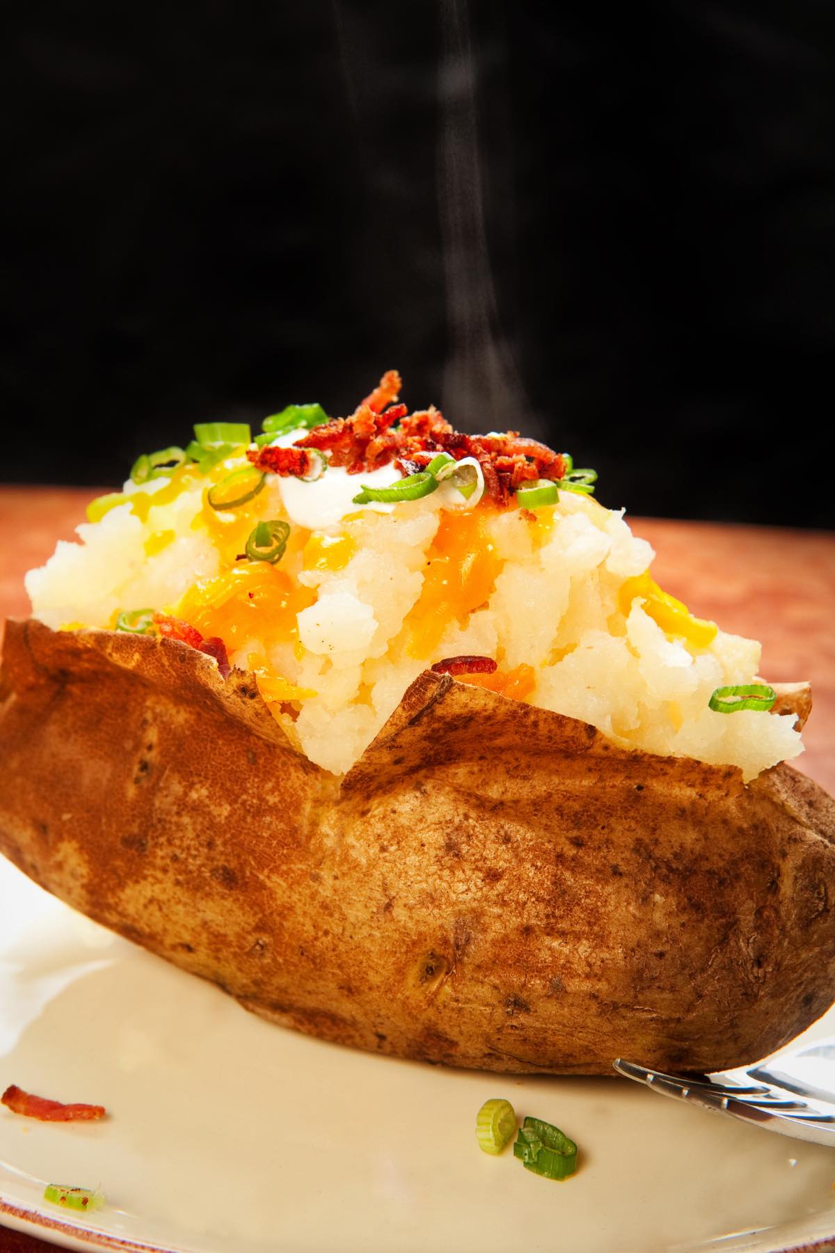 A fluffy baked potato with favorite toppings including butter, bacon bits and green onions