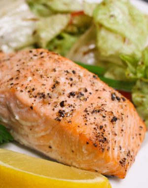 Serving of portion-size baked salmon fillet with a side salad on a serving plate with a lemon wedge