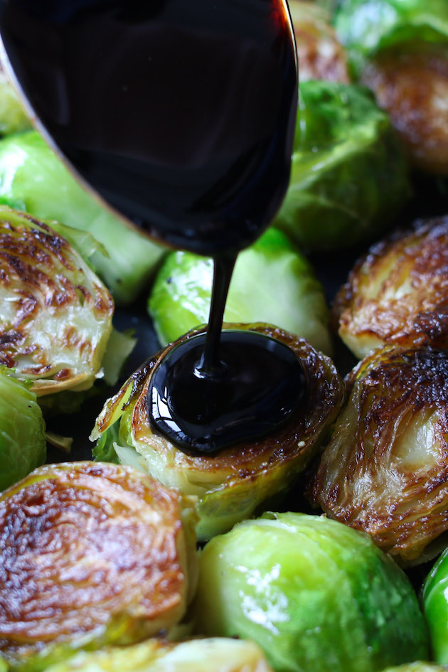 Homemade balsamic glaze drizzled onto caramelized Brussel sprouts from a spoon, adding extraordinary sweet and tangy flavor
