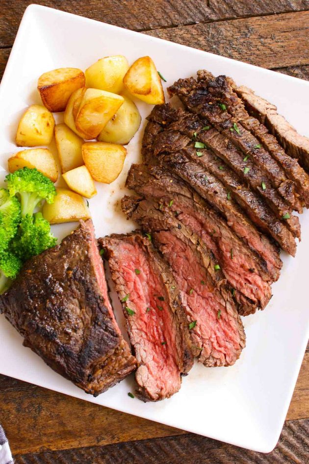 Sliced vacio steak on a serving plate with sautéed potatoes and broccoli