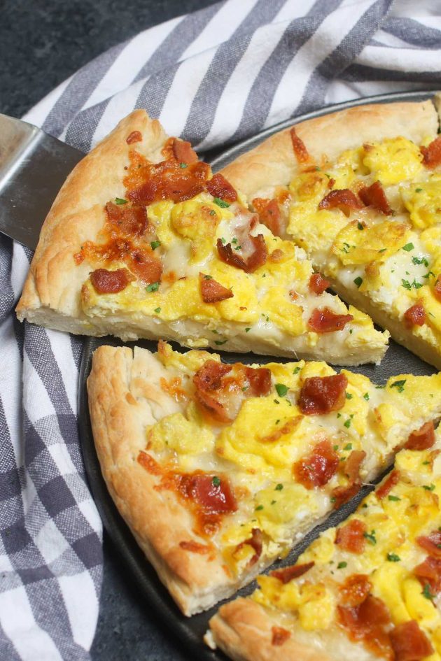 Easy Breakfast Pizza recipe begins with homemade pizza dough, topped with crisp bacon bits, scrambled eggs and mozzarella cheese.