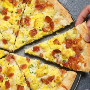 Easy Breakfast Pizza recipe begins with homemade pizza dough, topped with crisp bacon bits, scrambled eggs and mozzarella cheese.