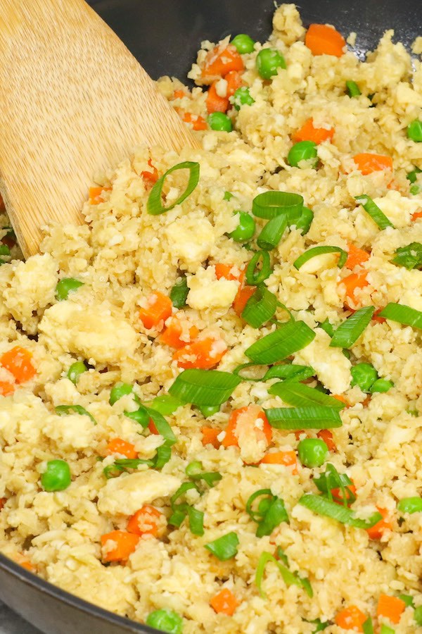 Delicious cauliflower fried rice with carrots, peas and scallions in a skillet ready to be served