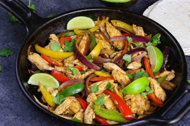 A cast iron pan with thin strip of chicken, bell peppers and onions ready to serve