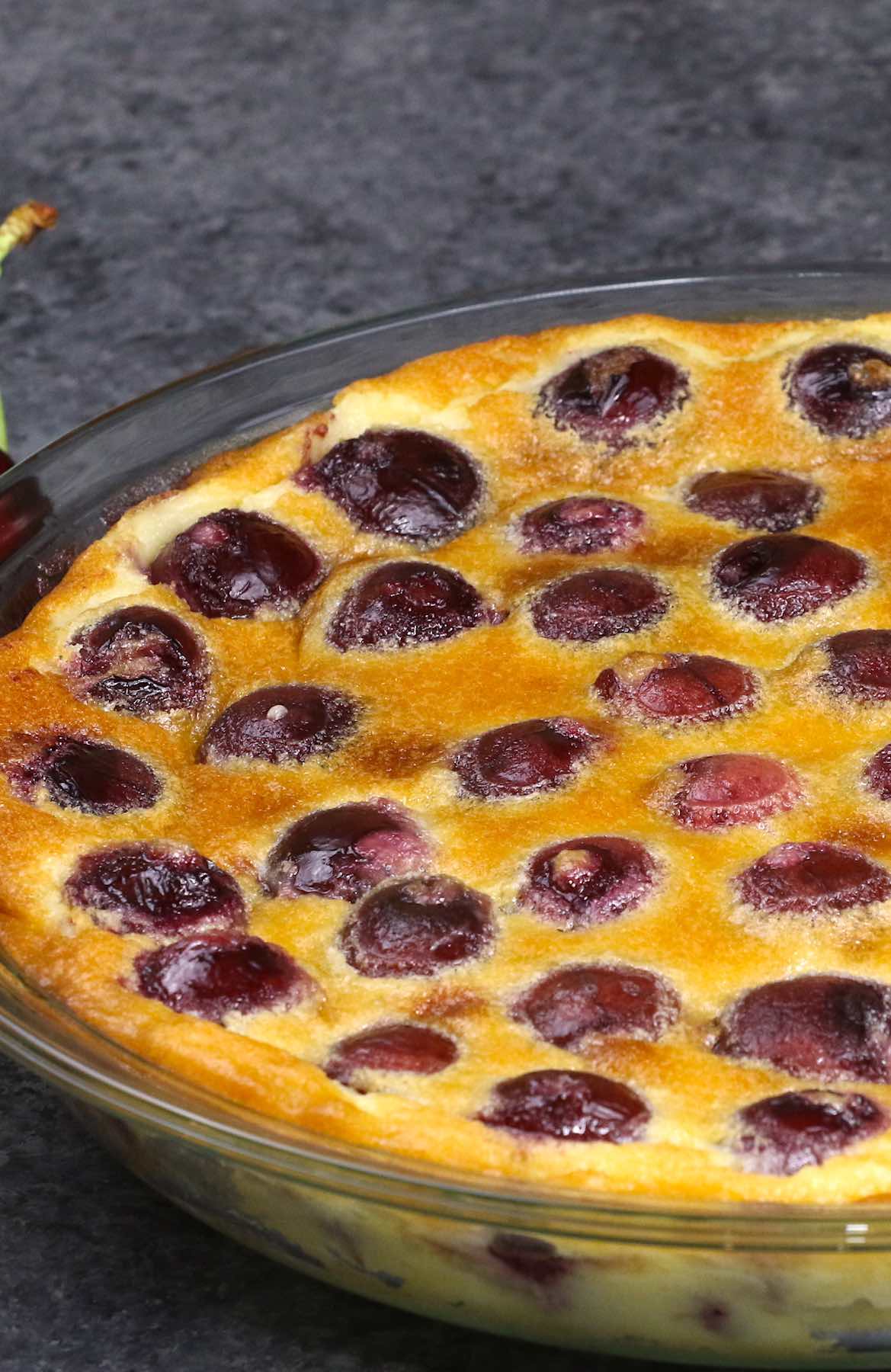 Closeup of a baked clafoutis aux cerises when done, showing the golden surface of the custard interspersed with cherries