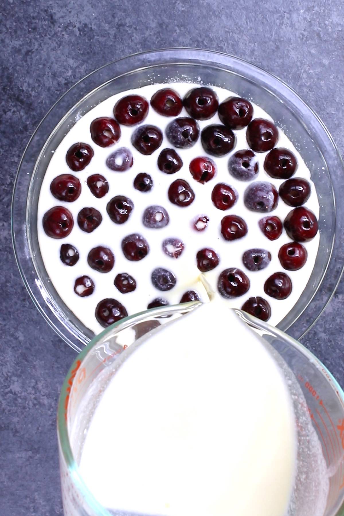 Overhead view of pouring batter on top of cherries when making a clafoutis