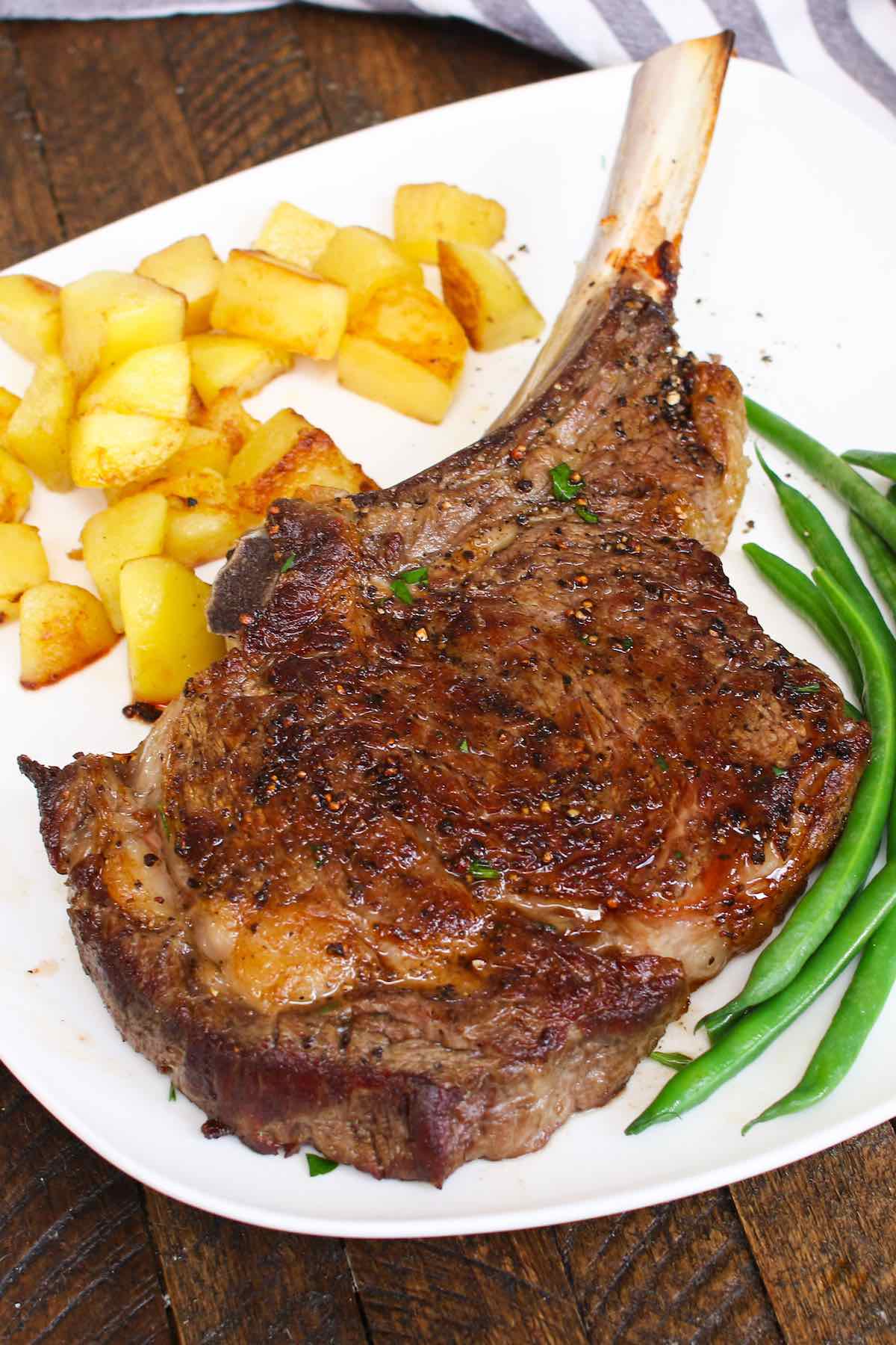 Cowboy steak cooked in the oven and served with green beans and sauteed potatoes for a delicious steak dinner