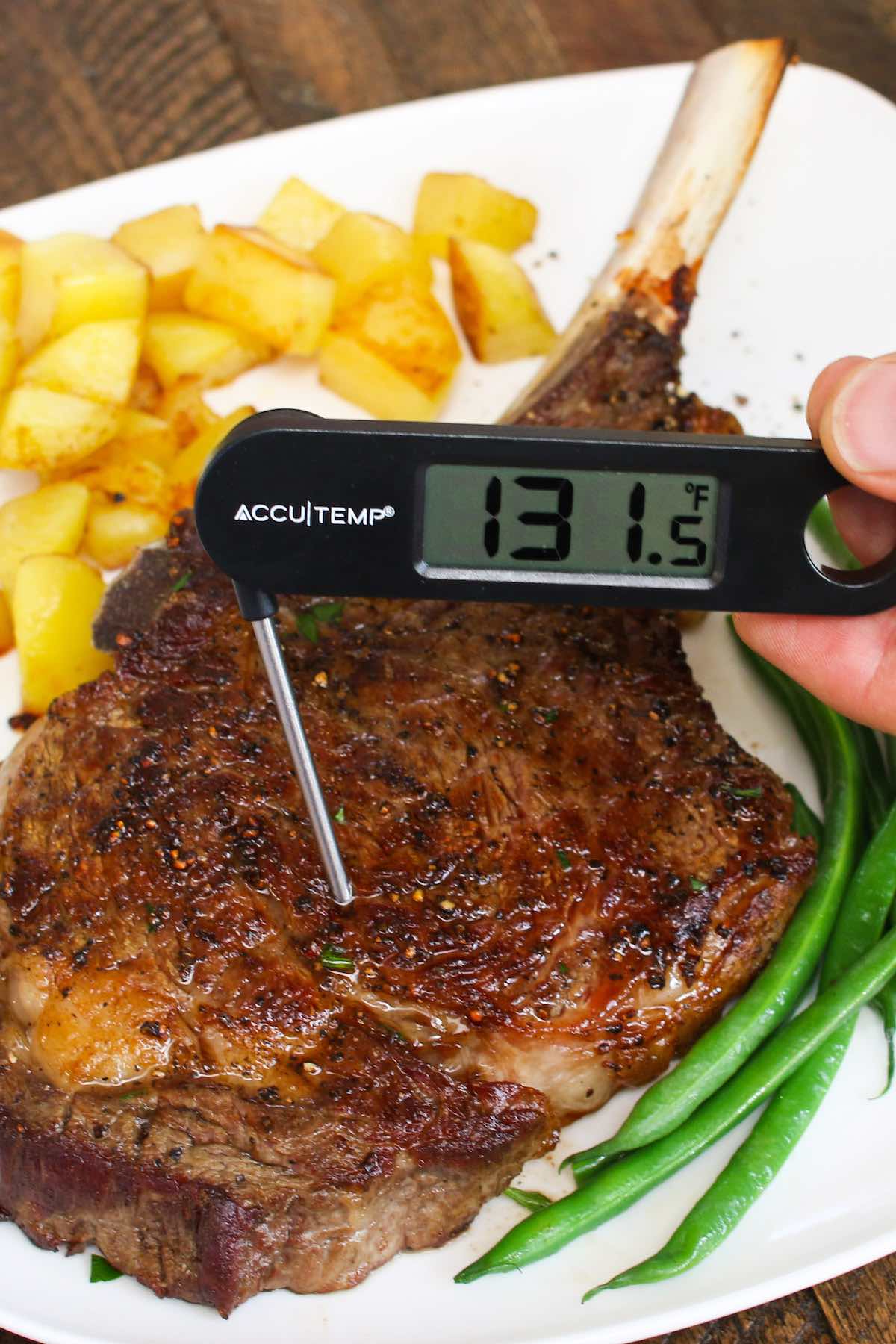 Checking doneness of a cowboy cut using an instant-read thermometer inserted into the middle of the steak. The reading is 131°F indicating medium doneness