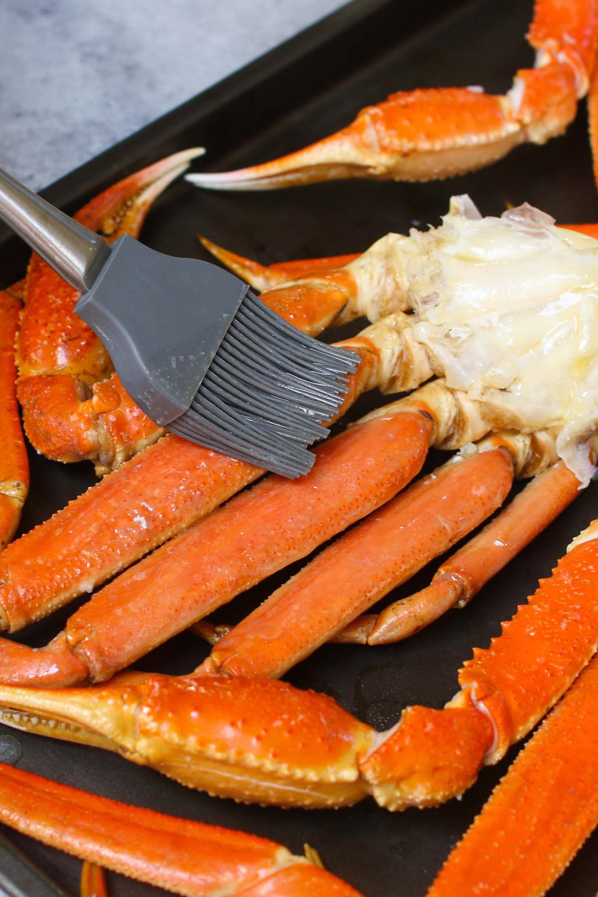 Brushing crab legs with melted butter on a baking sheet.
