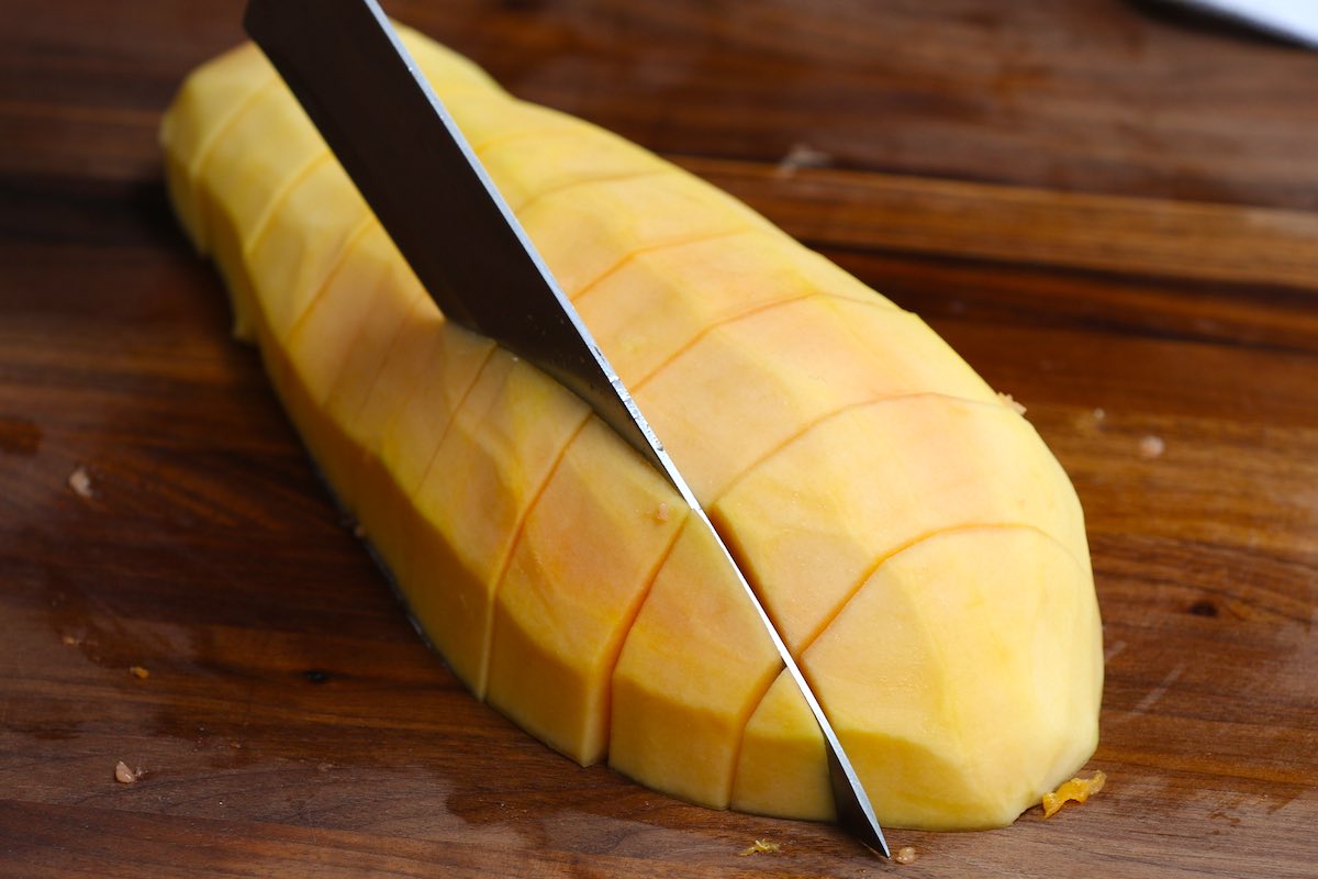 Cutting a peeled papaya into chunks using a large knife