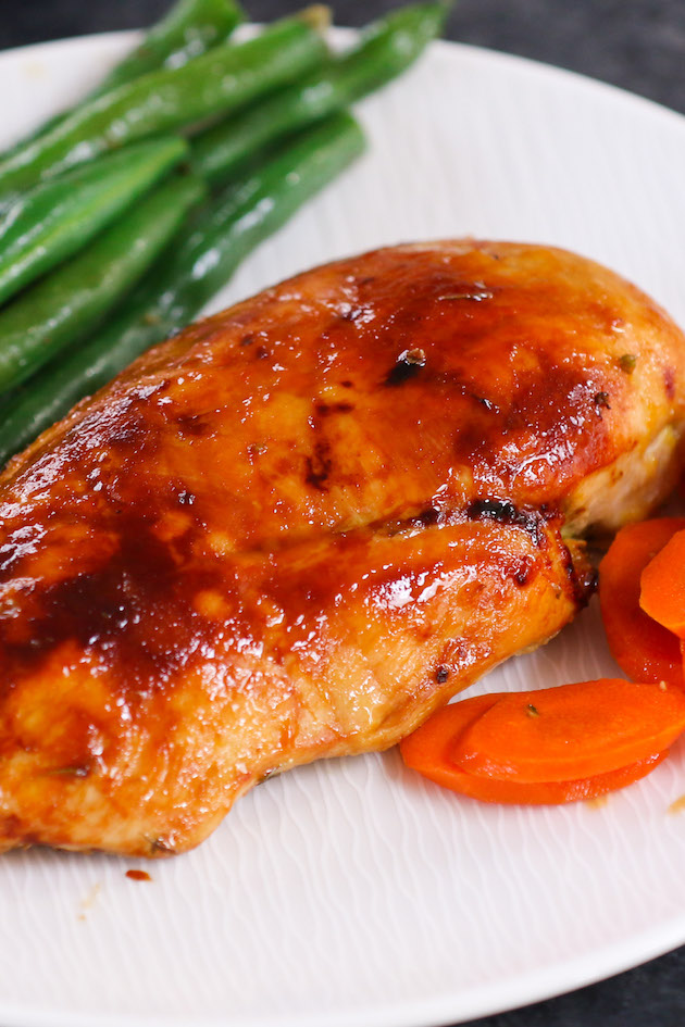 Baked chicken breast on a serving plate with carrots and green beans.