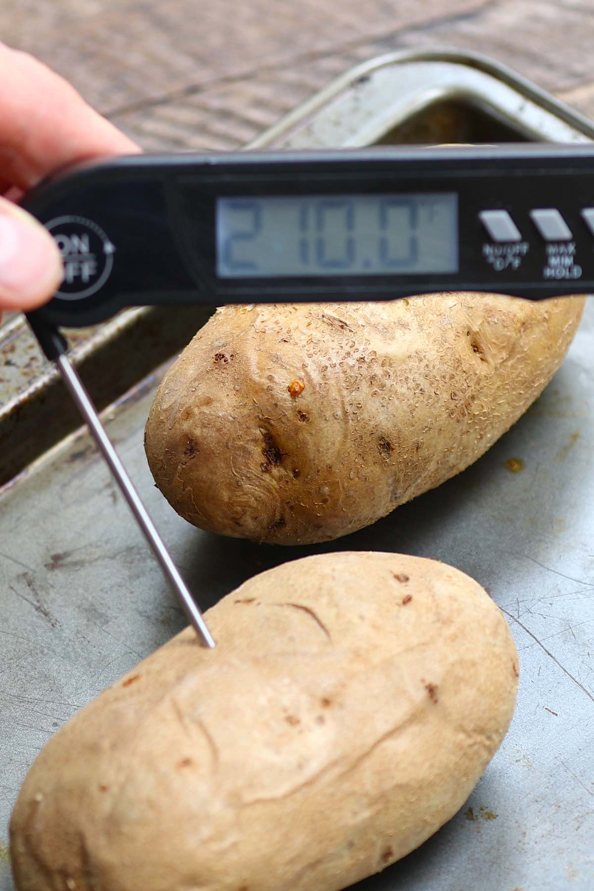 Inserting an instant-read thermometer into the middle of a potato to determine how long to bake a potato. It's done at 210 degrees F.