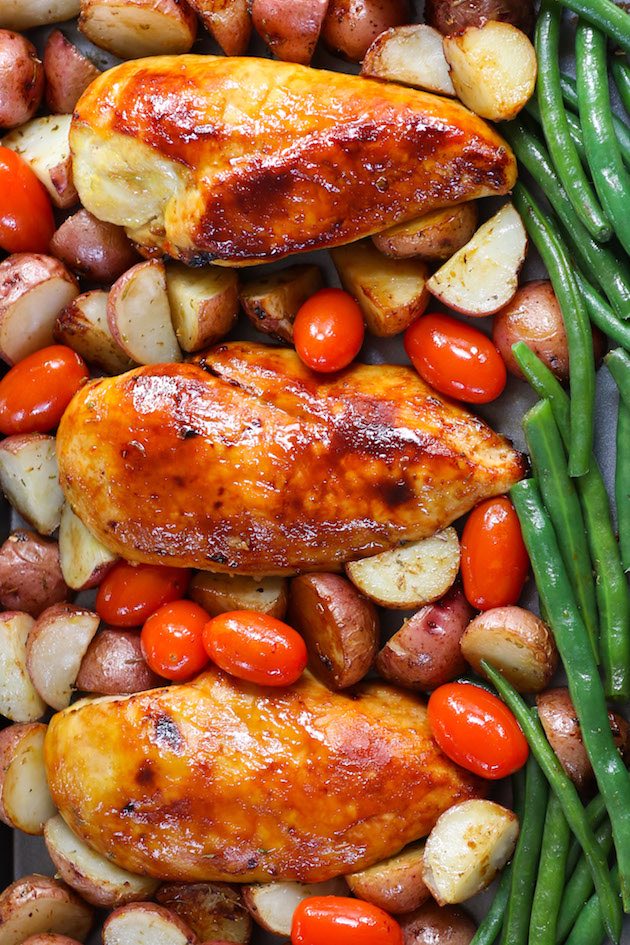 Baked chicken breasts with potatoes, green beans, tomatoes on a sheet pan.