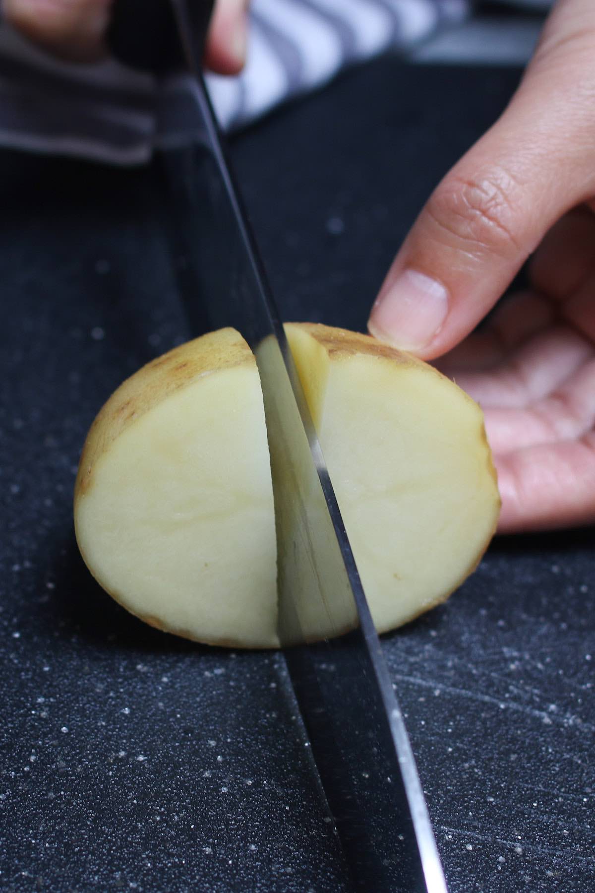 Cutting a raw white potato into quarters with a chef's knife for faster boiling