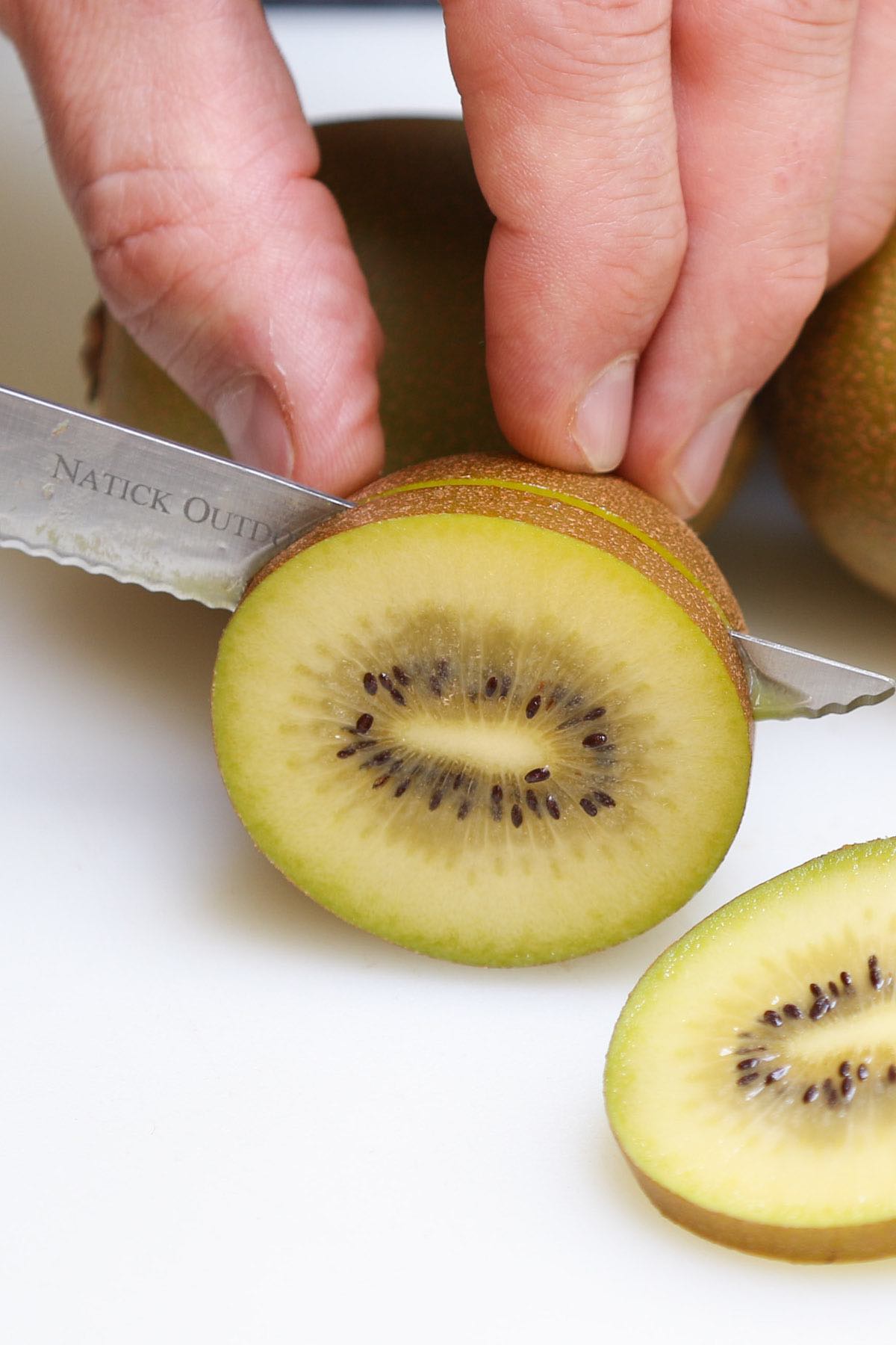Slicing a kiwi widthwise with a paring knife while leaving the skin on