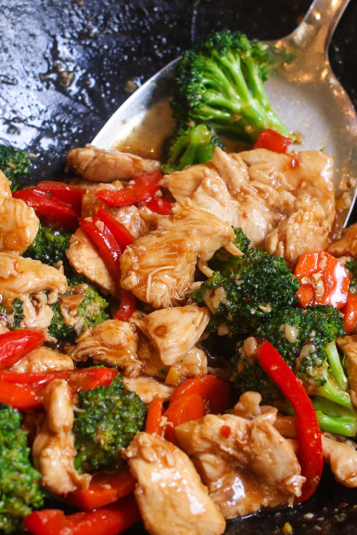 Closeup of Hunan chicken in a wok before serving showing juicy slices of chicken with broccoli, carrots and red bell pepper in a spicy hunan sauce