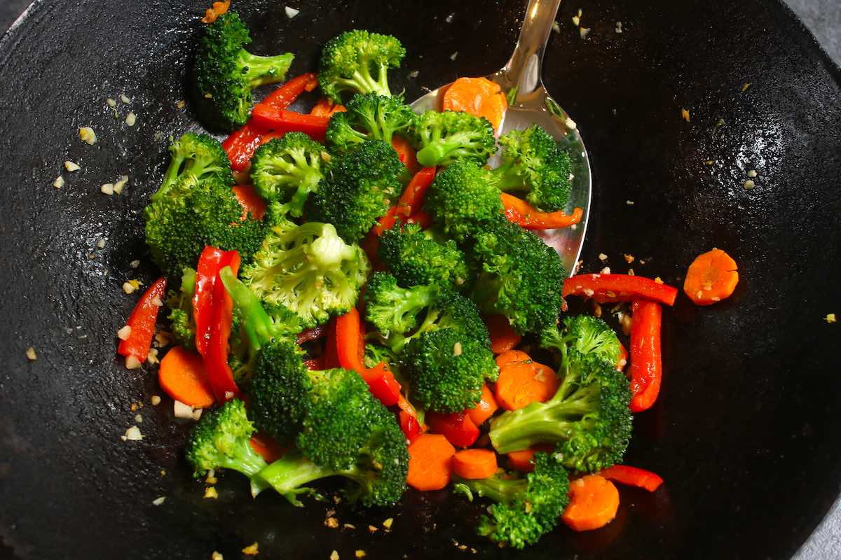 Stir frying broccoli, carrots, red bell pepper and minced garlic in the wok.
