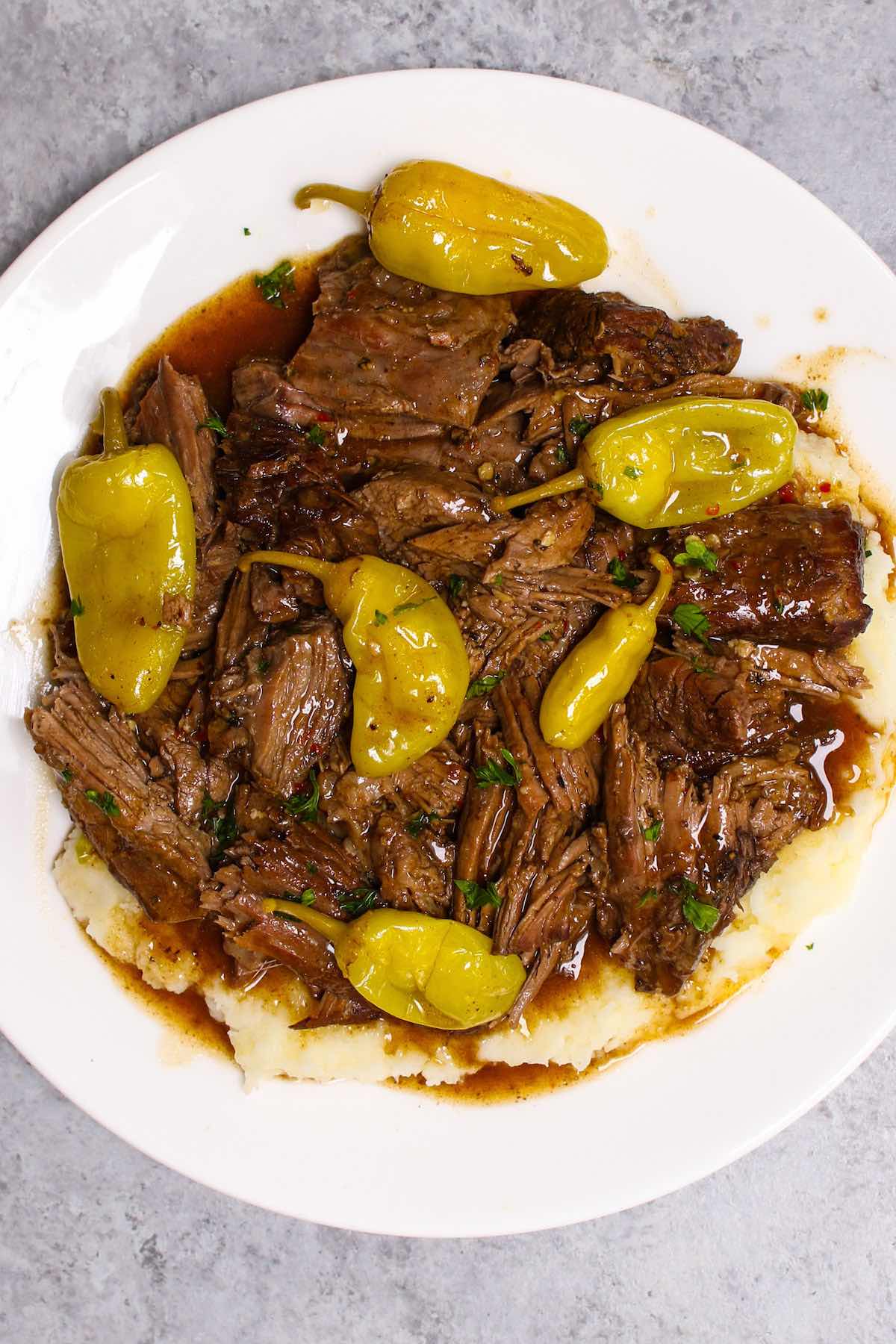 Instant pot Mississippi pot roast served over mashed potatoes, drizzled with delicious gravy on a white plate.