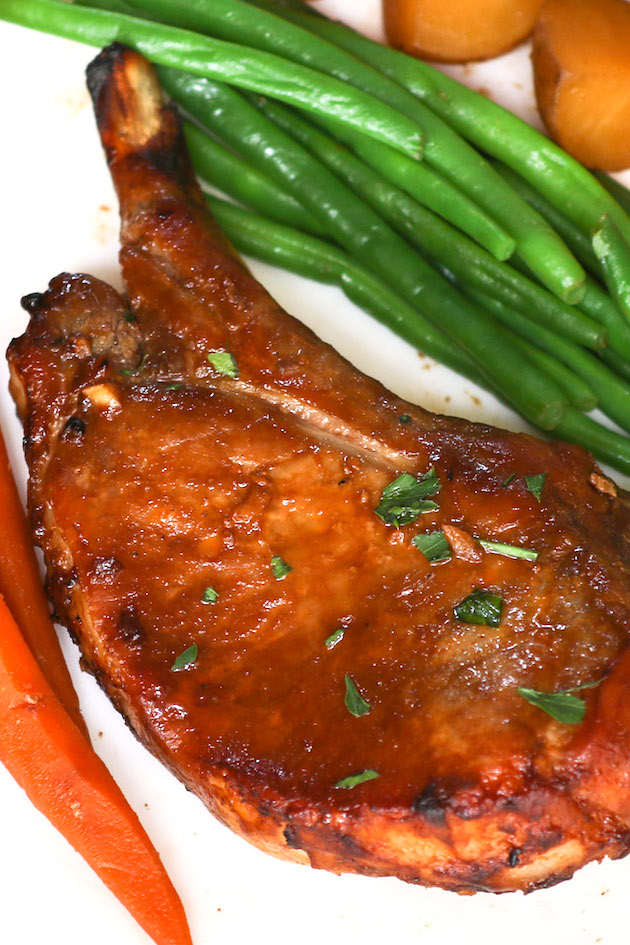 Instant pot bone-in pork chops served on a white plate with carrots and green beans.
