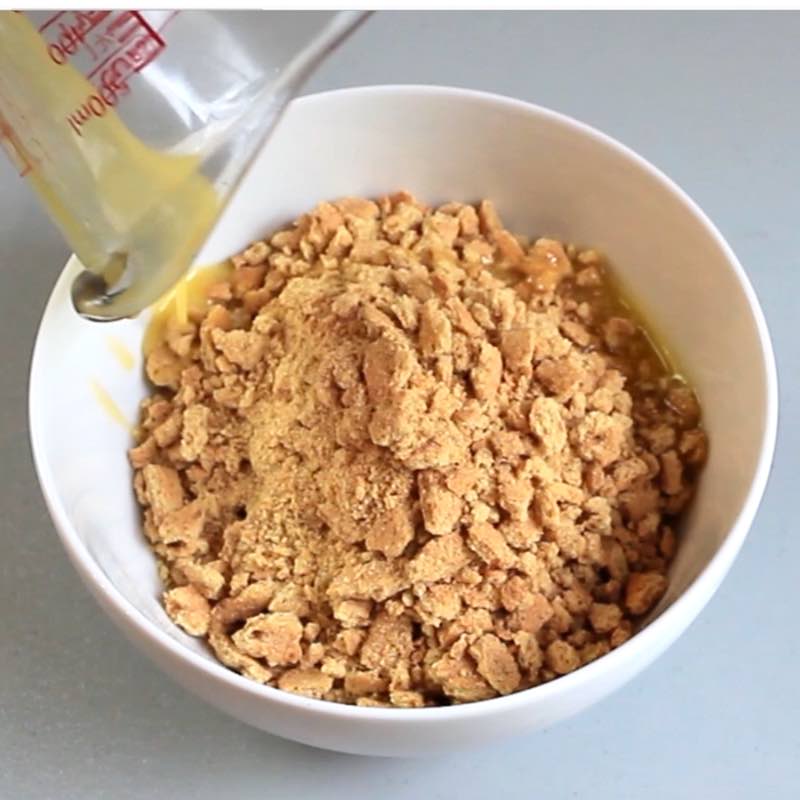 Making a graham cracker crust by combining crushed graham crackers with melted butter in a bowl