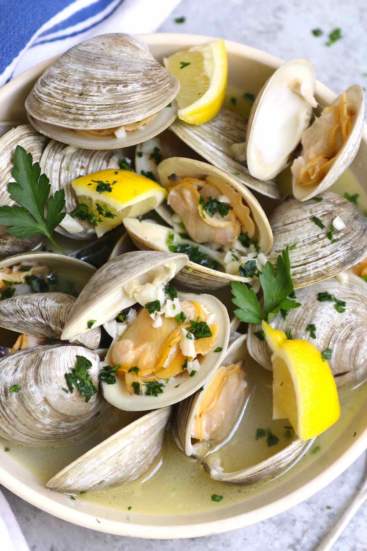A serving of little neck clams with lemon wedges and fresh herbs