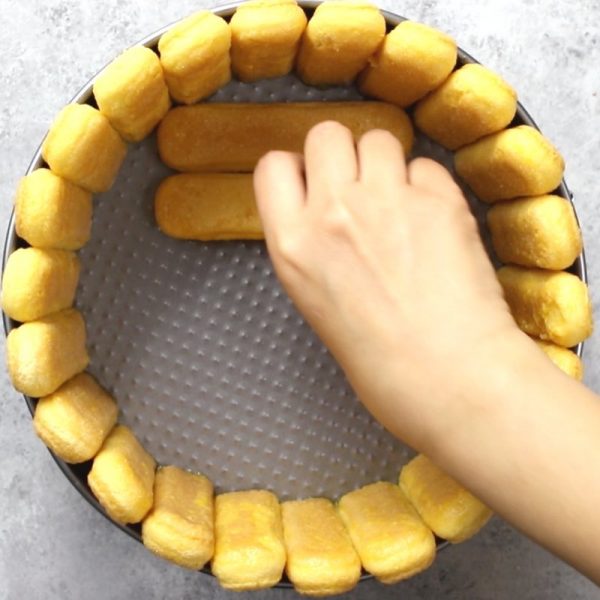 This photo shows how to arrange ladyfingers inside of a cake mold to make a Mango Cheesecake Charlotte