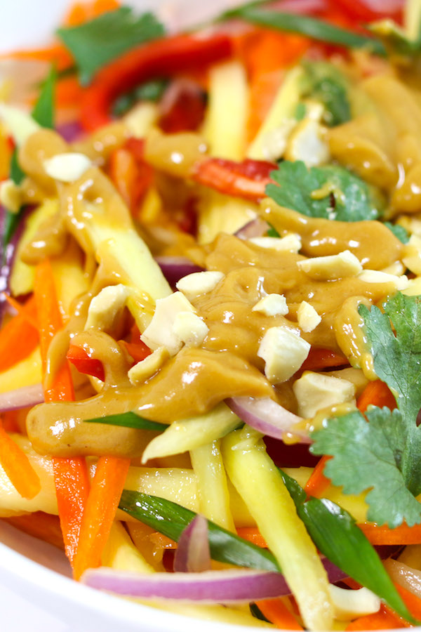 Closeup view of mango salad topped with chopped peanuts and drizzled with peanut dressing