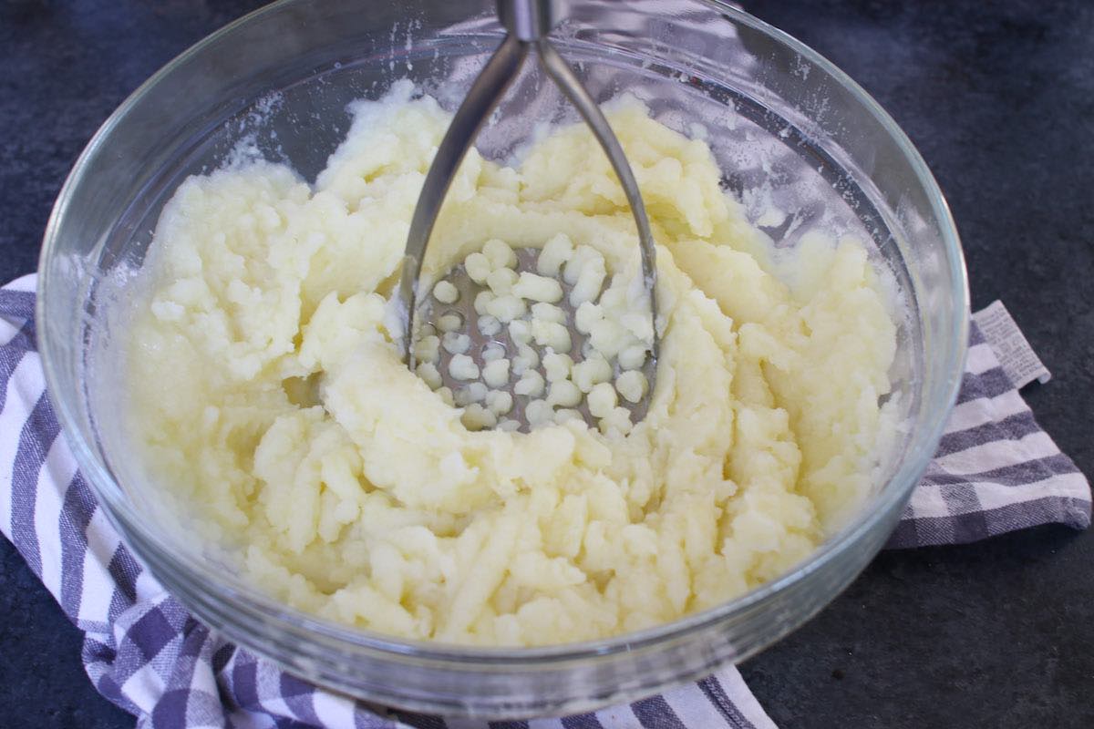 Using a potato masher to mash potatoes with butter and milk in a bowl after microwaving