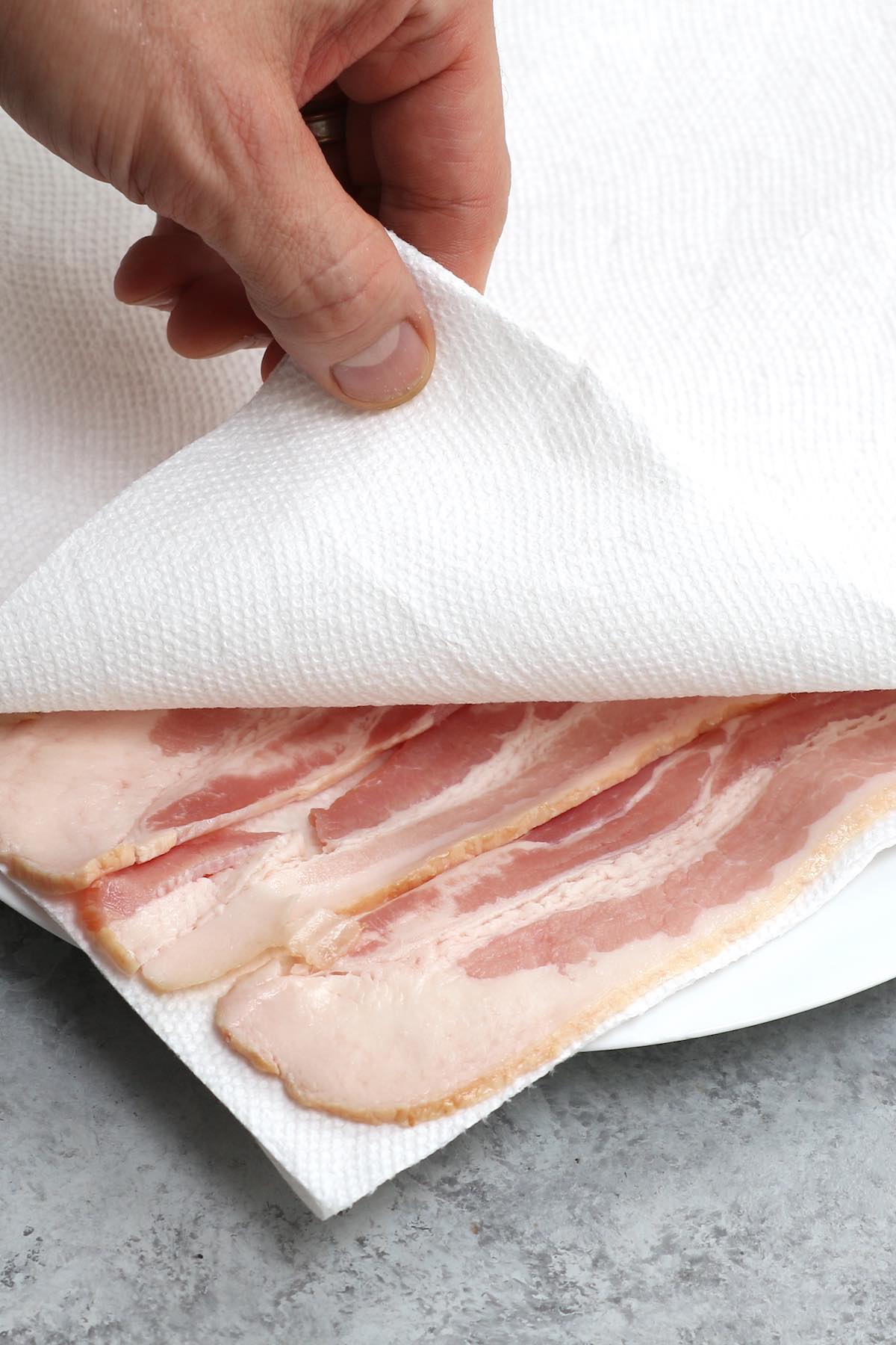 Placing strips of raw bacon between layers of paper towels in a single layer before microwaving