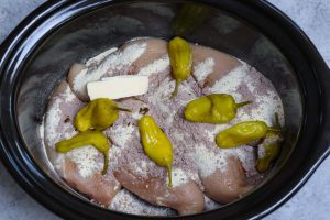 Crock pot with chicken breasts, au jus mix, ranch mix, pepperoncini peppers and butter