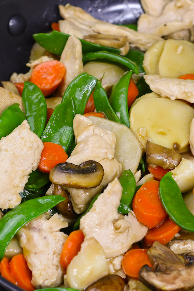 Stir fry chicken and vegetables in a pan.