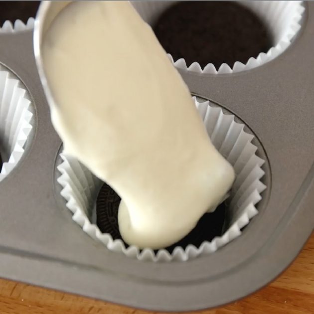 Mini Oreo Cheesecake Cupcakes - this photo shows adding the cheesecake filling on top of an oreo in a paper cupcake cup