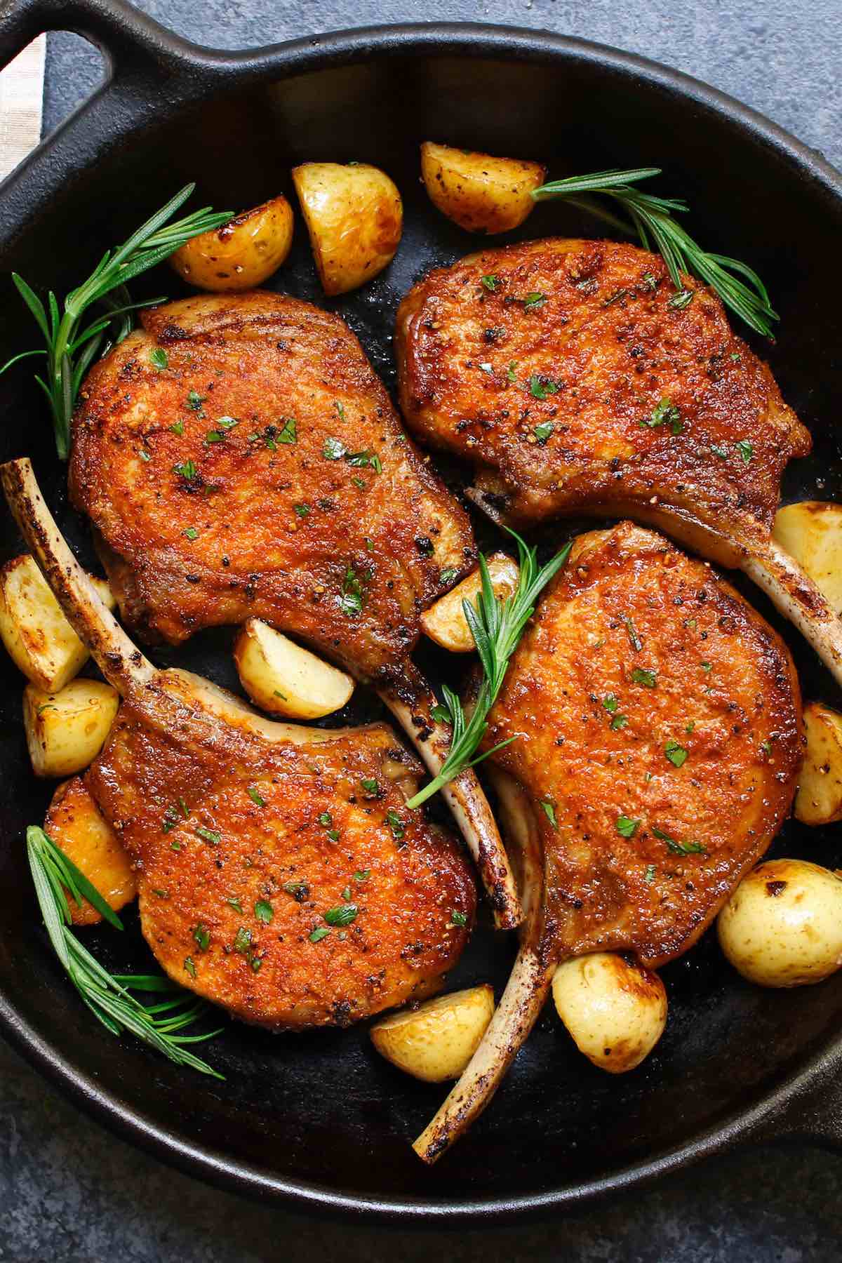Tender and juicy pan fried pork chops in a cast iron skillet with sprigs of fresh rosemary and sauteed potatoes