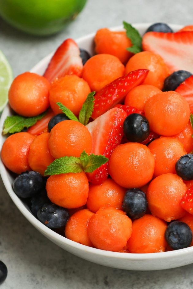A bowl of freshly cut papaya with berries and mint sprigs