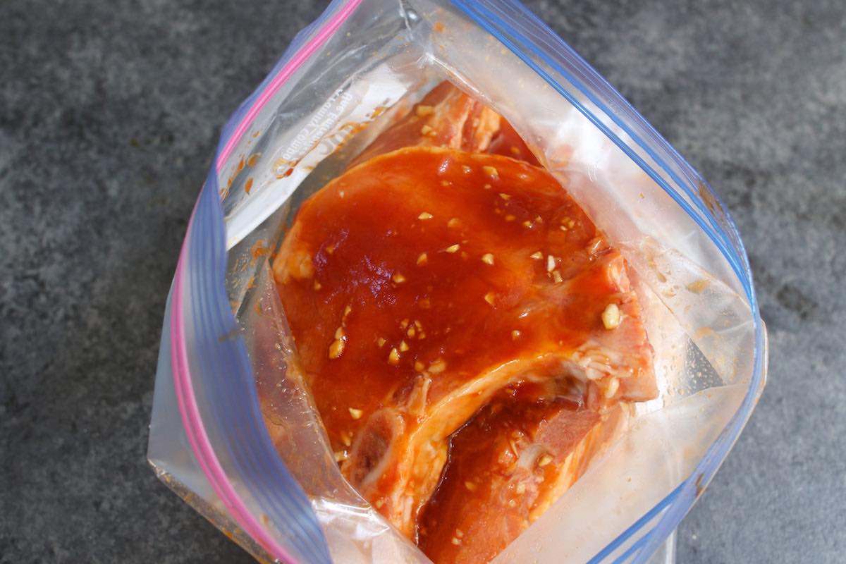 Pork chops soaking in the marinade in a resealable plastic bag.