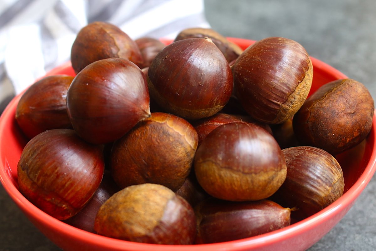 Fresh raw chestnuts in a red bowl.