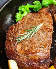A traditional rib eye steak in a cast iron pan after being pan seared, with broccoli and sauteed potatoes on the side ready for serving