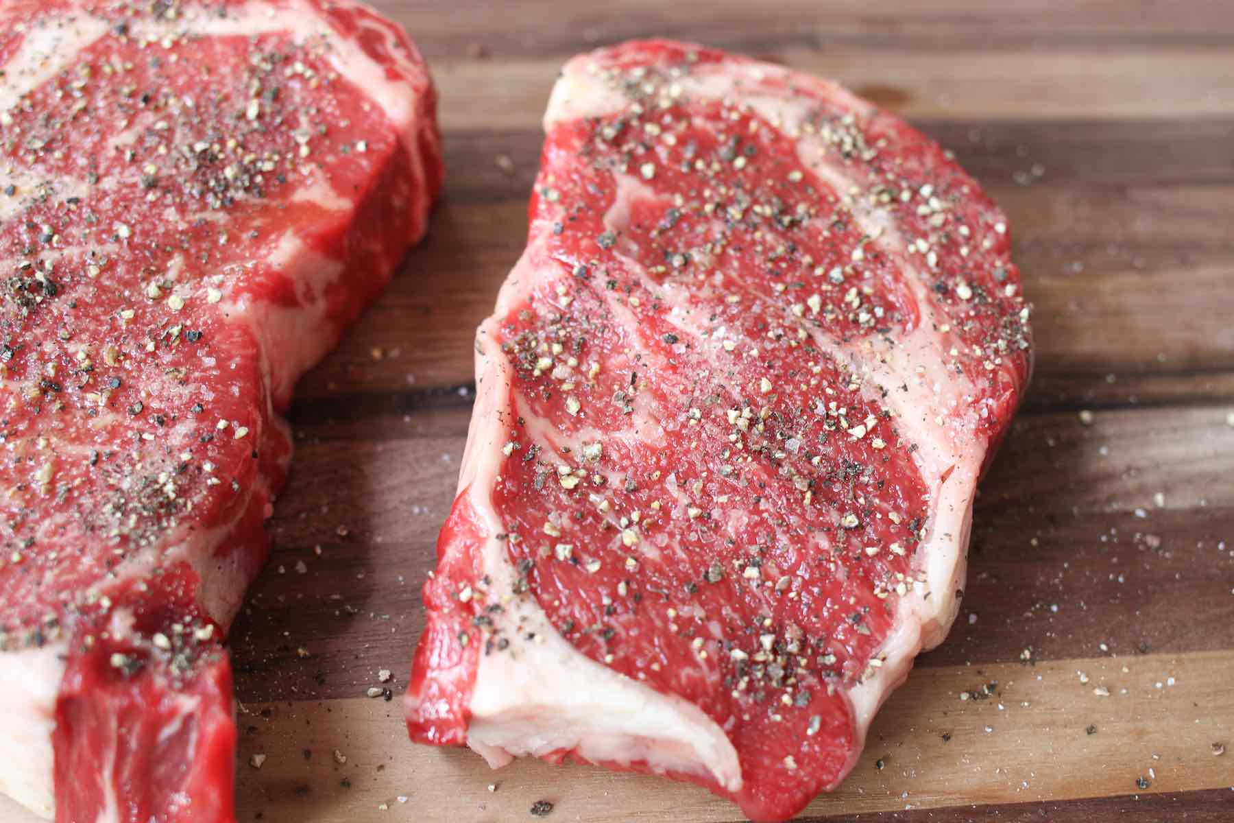 Closeup of seasoning of coarse salt and black pepper on a rib eye steak before cooking
