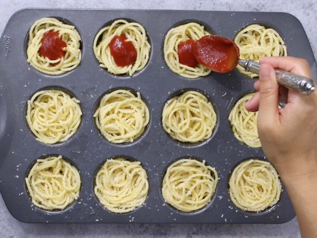 Adding the sauce to the spaghetti in a muffin tin when making Spaghetti Meatball Cups