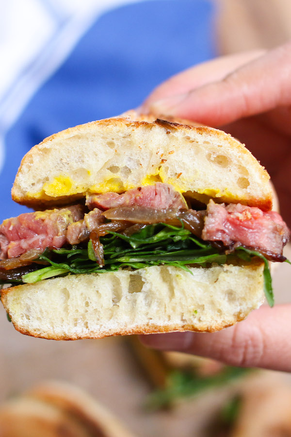 This steak sandwich recipe involves pan-seared steak, caramelized onions, arugula and mustard. There is a good mix of protein, vegetables and dressing piled between carbs.