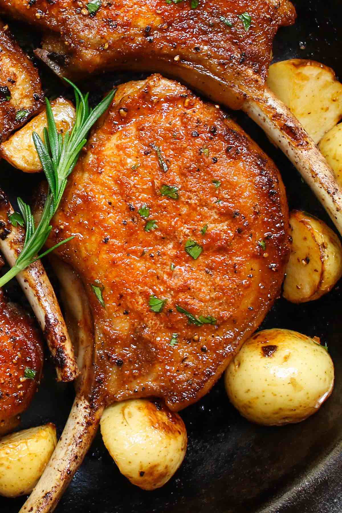 Closeup of stove top pork chops with a perfect golden crust and sauteed potatoes on the side
