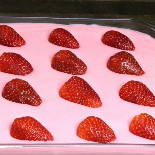 Here is a close-up photo of halved fresh strawberries floating beautifully on top of the filling in strawberry jello cake before the mirror glaze is added