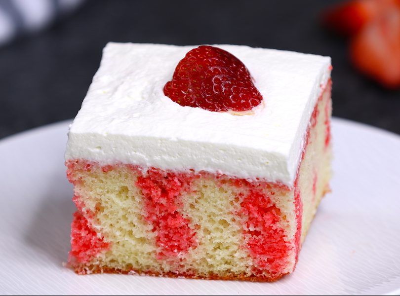 A piece of Strawberry Jello Poke Cake on a serving plate showing beautiful streaks of strawberry jello in the cake layer - it's a delicious dessert that's easy to make with a few simple ingredients