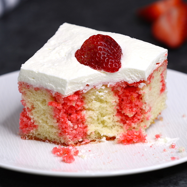 This photo shows a serving of strawberry poke cake that has been partially eaten and shows the beautiful contrast of red and white colors in the cake layer and crumbs on the plate