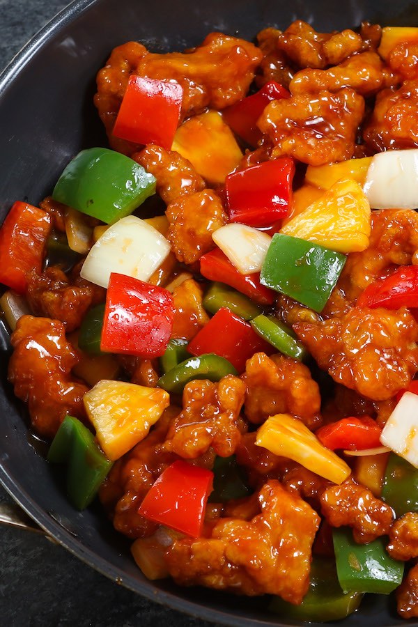 Crispy chicken pieces with colorful bell peppers, onion and pineapple in a skillet