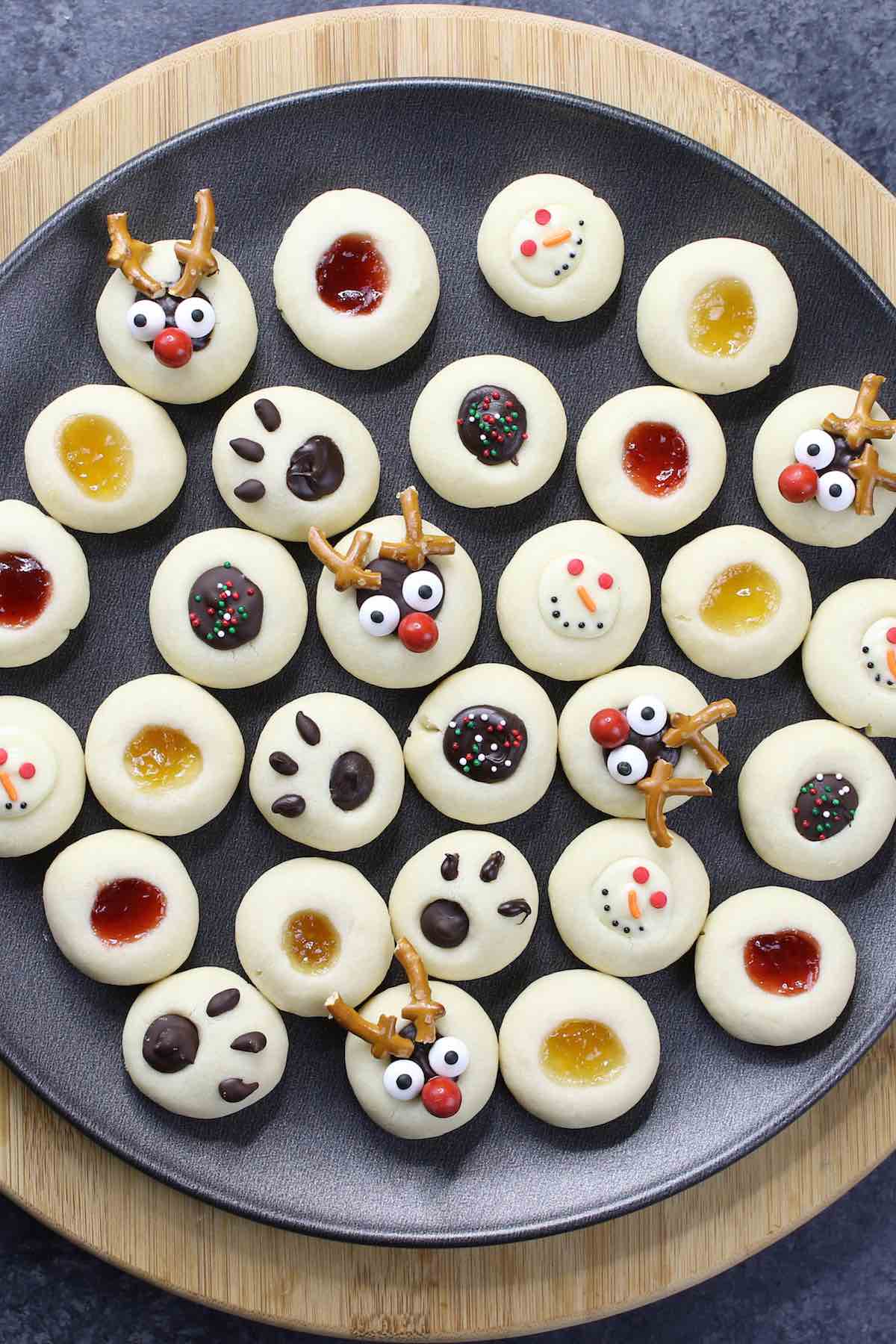 Mixture of jam thumbprint cookies and Christmas chocolate thumbprint cookies on a dark plate.