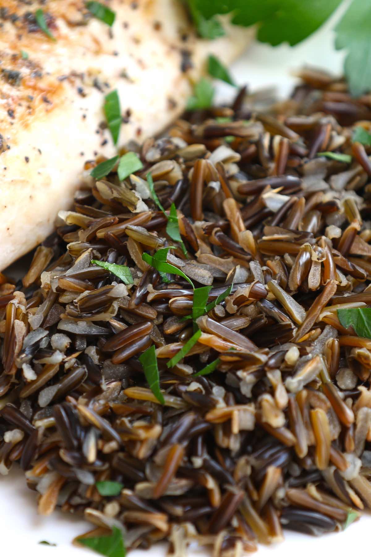 Closeup of wild rice as a side dish for baked chicken breast, all garnished with fresh parsley