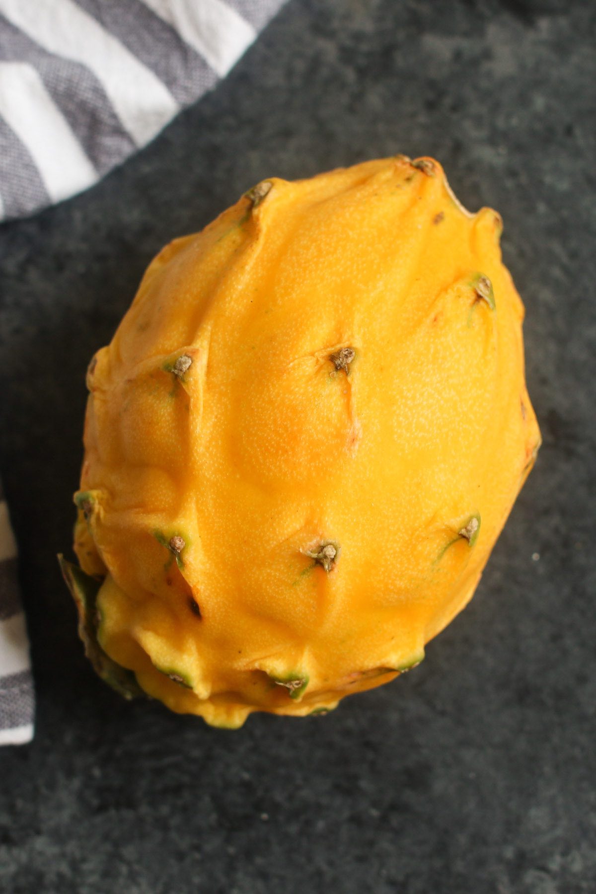 A whole yellow pitaya with its bright yellow color, oblong shape and knobby skin